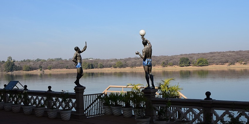 Sakhya Sagar Lake with a still water body, two statues holding lamps and a sandy shoreline