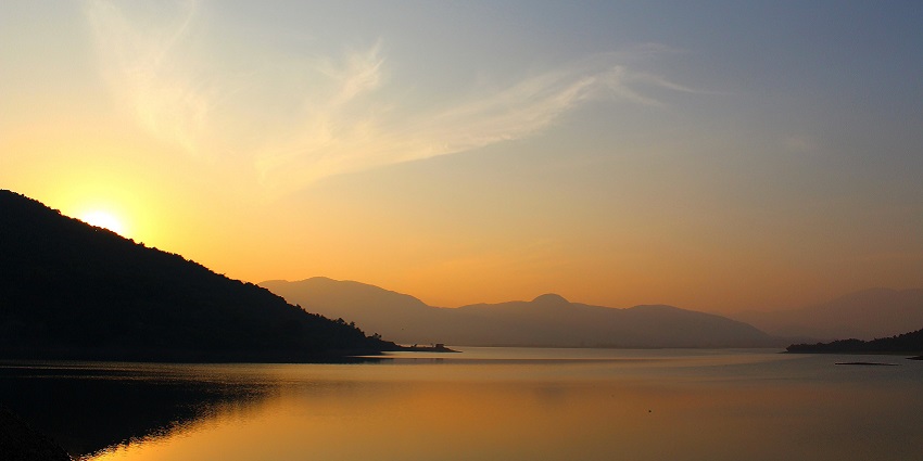 Salia Dam Lake with the sun setting behind the hills and hills reflecting on the lake