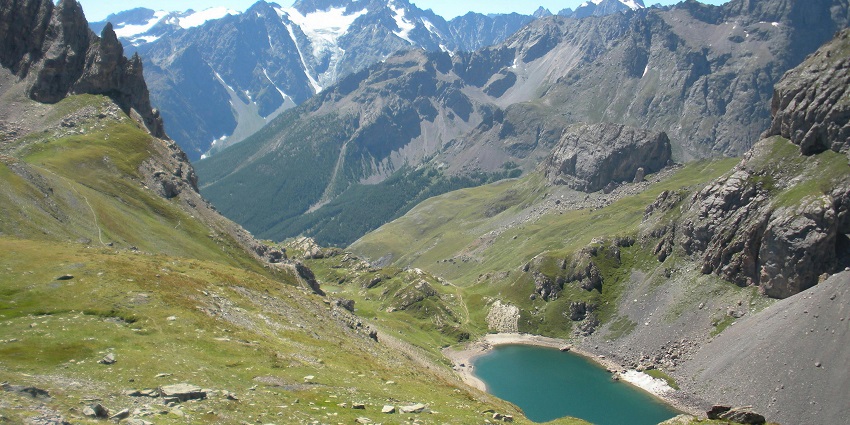 Lake from above, surrounded by big green hills and mountains with peaks covered in snow