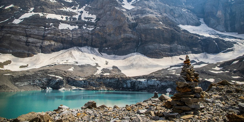 Lake surrounded by rocky shores and a pile of stones near the lake with hills in the back.