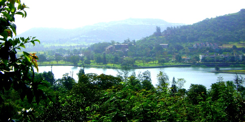 A scenic view of Saputara, Gujarat, with lush green hills, a lake, and a cloudy sky.
