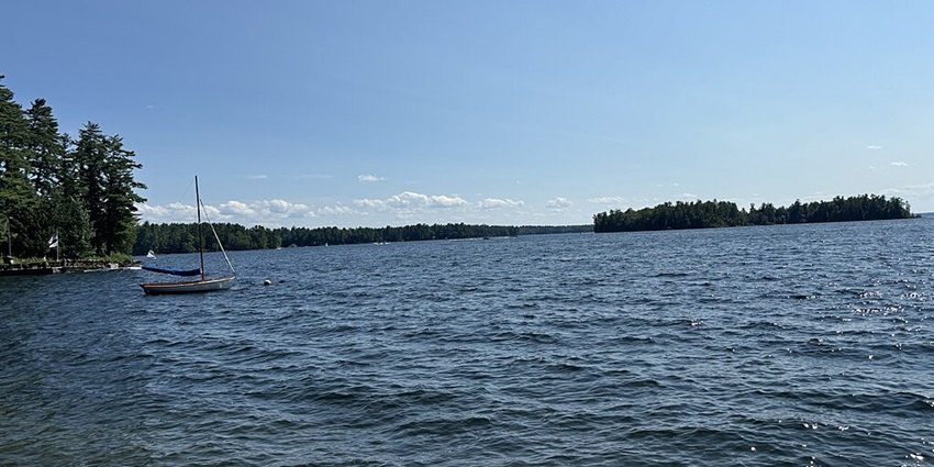 A small yacht sails in the wavy waters of Sebago Lake in Cumberland County, Maine.