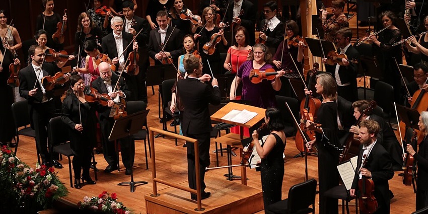 Indianapolis Symphony Orchestra performing in a hall with a large audience present.
