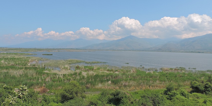 Landscape of a small Prespa lake with a green shoreline and hills in the background