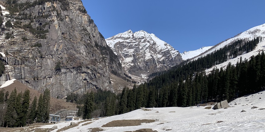An image of the snow-covered landscape of Sethan, Himachal Pradesh, with tall pine trees, rocky mountains.