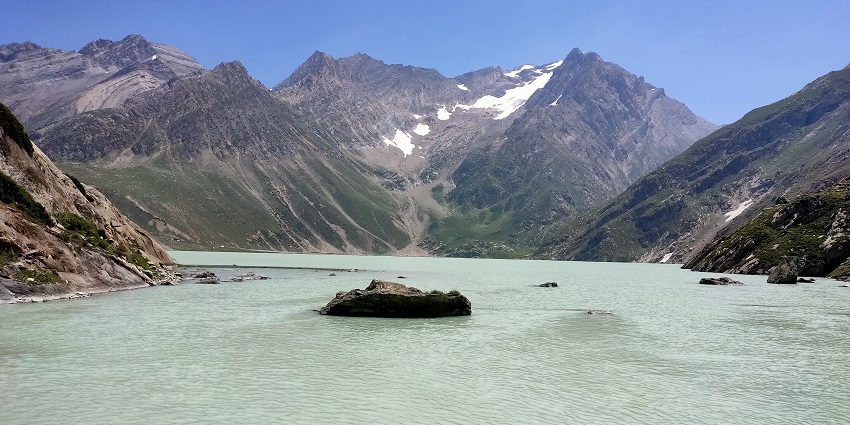 A scenic landscape of the Sheshnag Lake with rocky and snow-covered big mountains