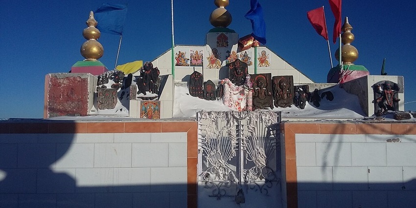 Shikari Devi temple with multiple blue and red flags, statues and paintings of Hindu gods.