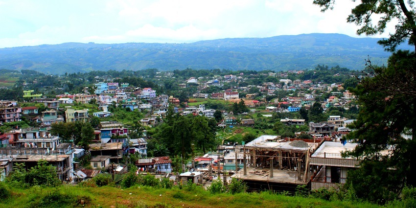An image showing the town of Shillong, Meghalaya, with rolling hills and scattered buildings.