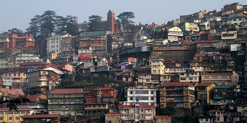 An image of the cityscape of Shimla, surrounded by misty hills and autumn foliage.