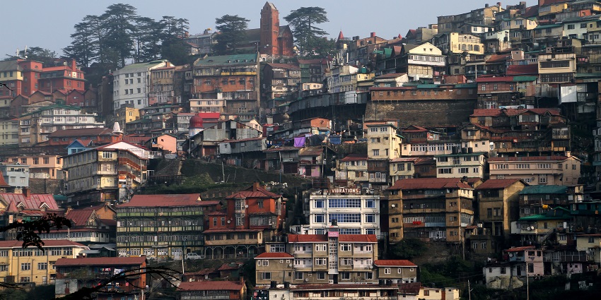An image of the cityscape of Shimla, surrounded by misty hills and autumn foliage.