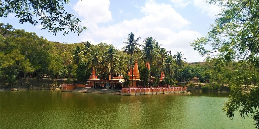Lake with a green water body and a bright, colourful temple surrounded by trees