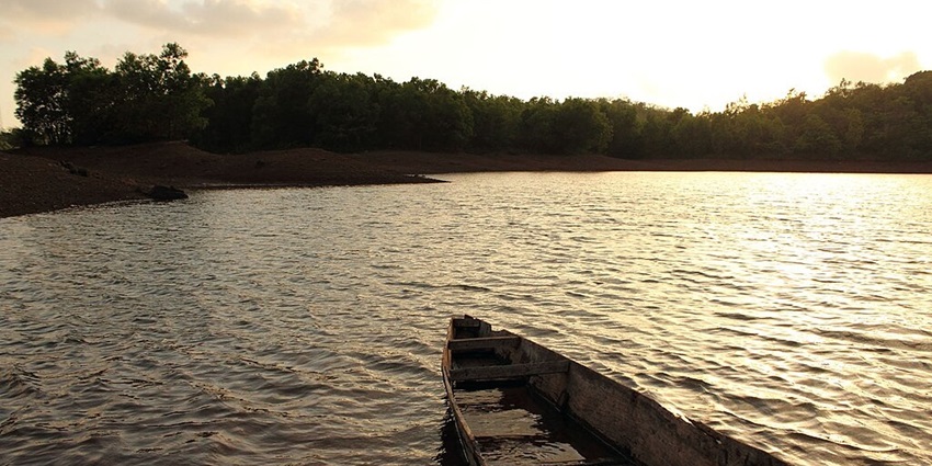 Lake with a bright sun in the back and an old wooden boat partially filled with water