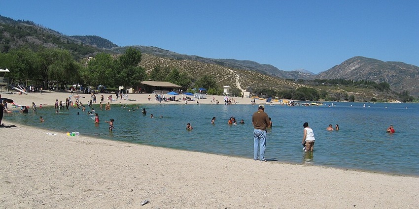 An image of Silverwood Lake with people swimming in the lake and lying on the shoreline