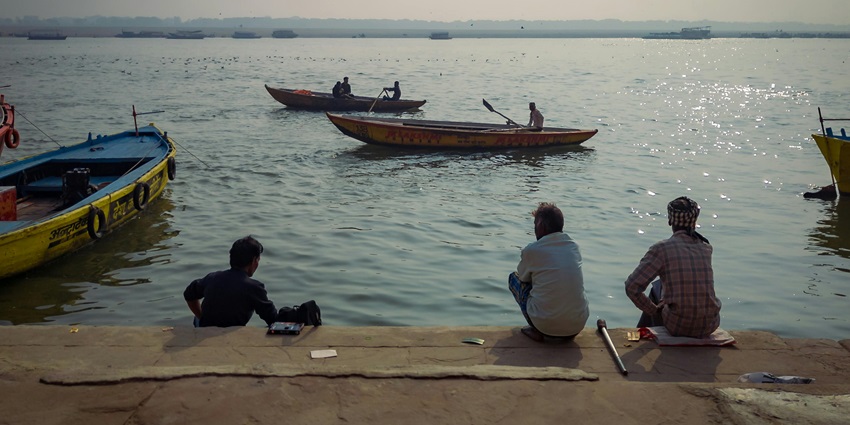 Image of people sitting on the ghat and with boats in the river resembling Simaria Ghat