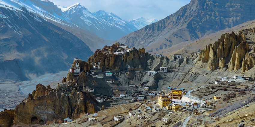 An image of the Spiti Valley’s mountainous landscape with a river winding through a valley, snow-capped peaks, and terraced fields.