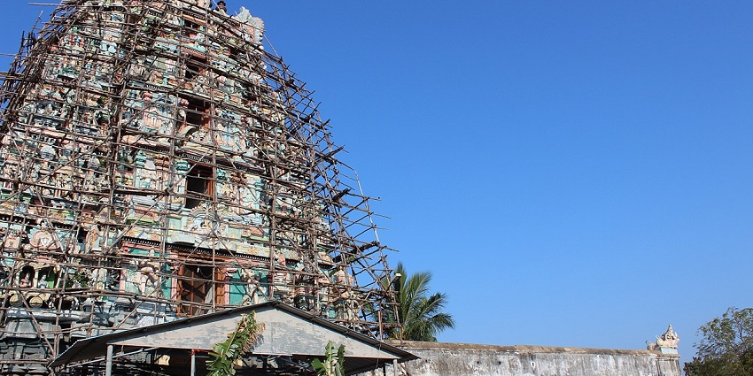 Gopuram of a temple with detailed Dravidian architecture, surrounded by bamboo sticks