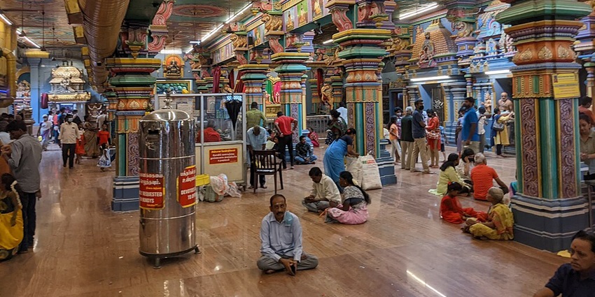 Interior of Vinayagar Temple with vibrant colourful pillars, walls and devotees sitting