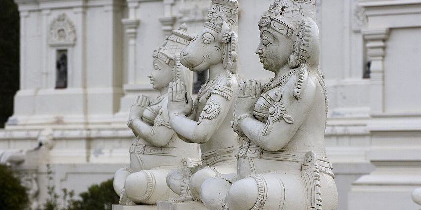 Statues of deities sculpted with white stone and the structure of Venkateswara temple behind