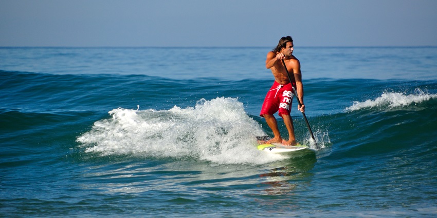 A view of a man enjoying stand-up paddle boarding across the calm waters of Puducherry.