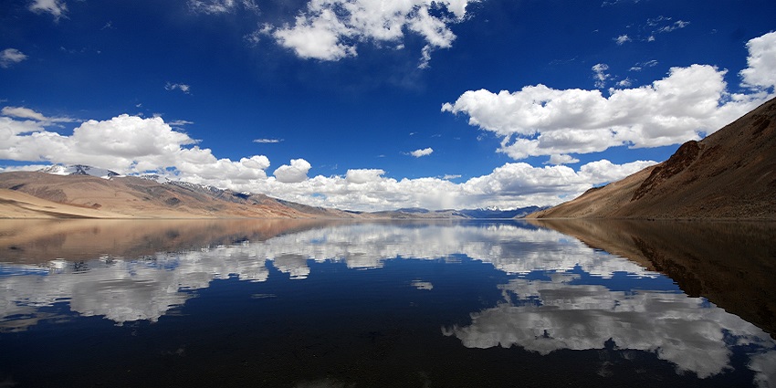 Lake with a perfect reflection of distant sandy brown mountains under a cloudy sky