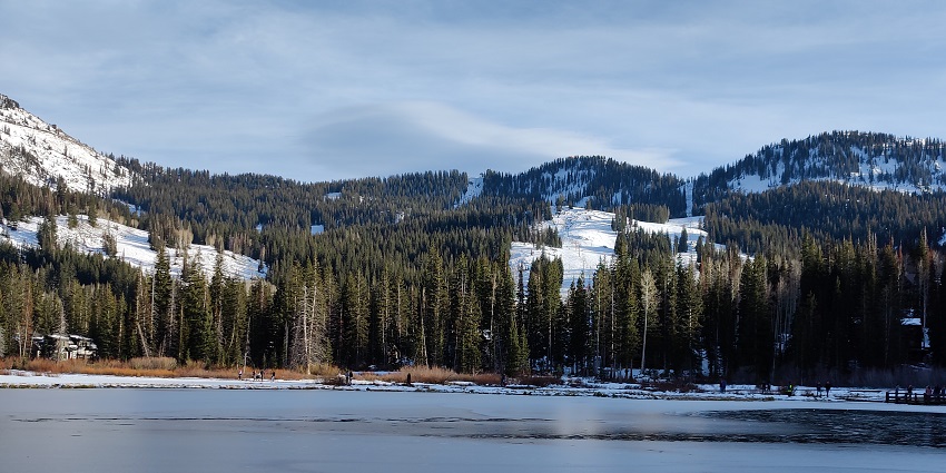 The green pine forest and the snow-white mountains enhance the beauty of the frozen lake
