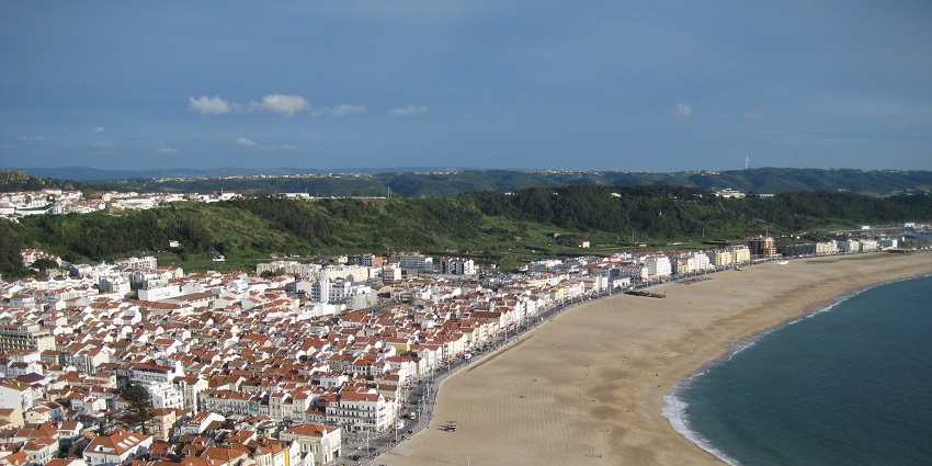 An aerial view of Nazare, Portugal, showing the red town, sandy beach, and coastline.