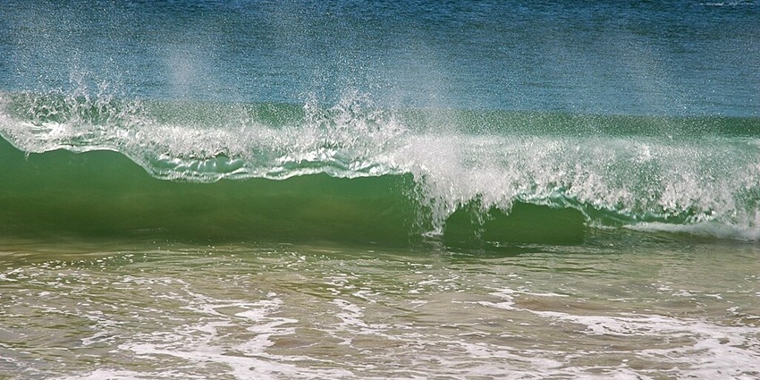 A vibrant green wave crashing on a sandy beach, with white foam and a clear blue ocean