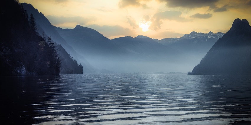 An image of Surinsar Lake with calm waters reflecting the surrounding forested hills.