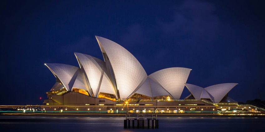 The Sydney Opera House illuminated at night, reflecting beautifully on the harbour waters