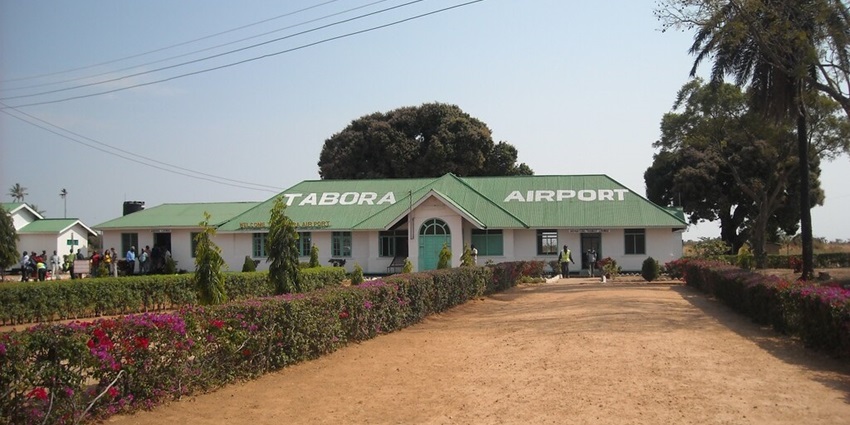 The front of the Tabora Airport building is green in colour with trees around and some people outside