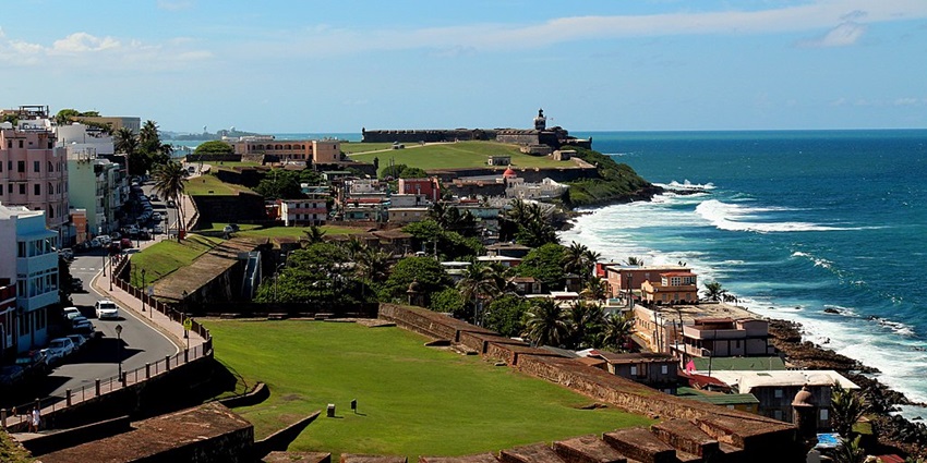 Coastal view of Old San Juan with El Morro in the distance and vibrant buildings.