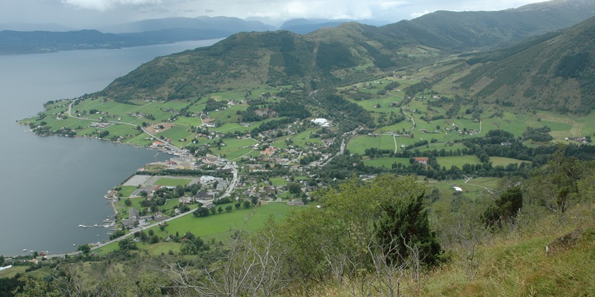 An Image of the Rosendal in Norway, featuring green fields, mountains and a fjord.