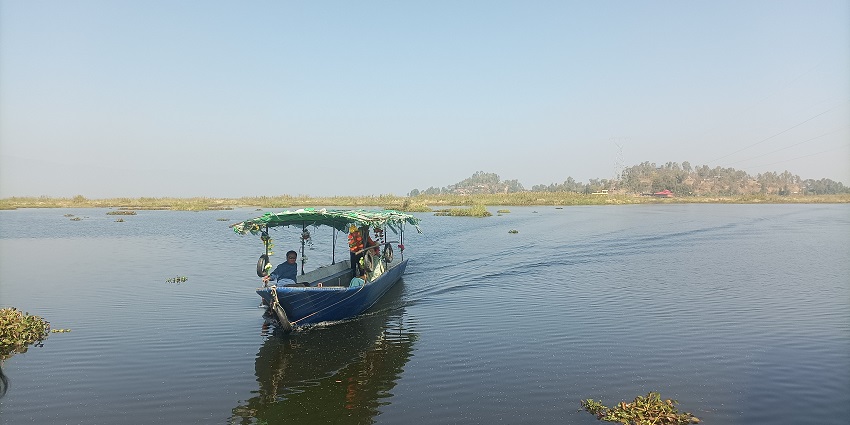 People in a boat on a lake with the water weeds coming out of the lake and a shore
