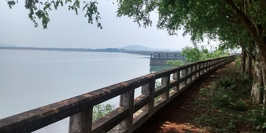 Lake with a large water body, concrete fences and distant mountains surrounded by greenery