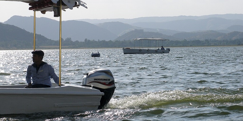 A man rides a motorboat while the boat’s propellers create trails on the lake’s surface.
