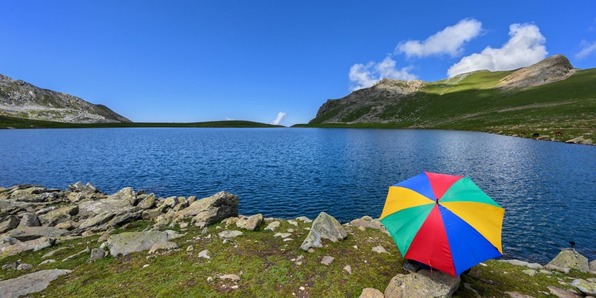 Tarsar Lake with a clear large water body, rocky shoreline and a multicoloured umbrella