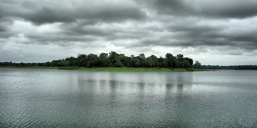 Dam reservoir with a large water body, green shorelines and green trees under a cloudy sky