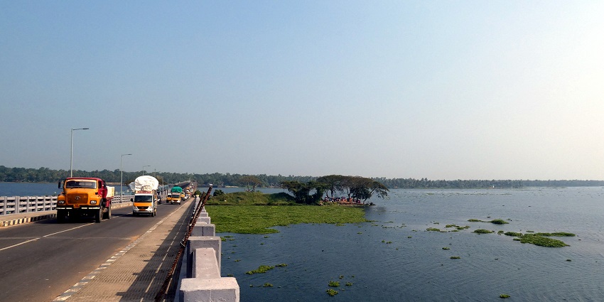 Thanneermukkom bund bridge with moving vehicles on the bridge and greenery in the back.