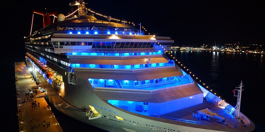 An image of a brightly lit cruise ship named Carnival Destiny docked at night with city lights in background