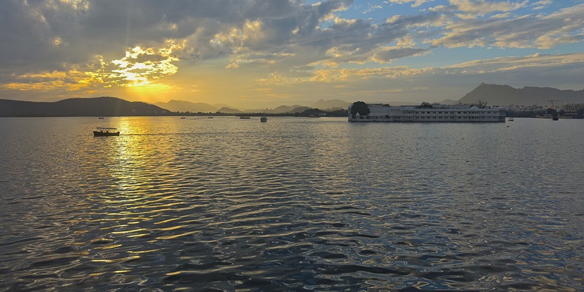 Golden hues of sunset reflecting on a tranquil lake, with silhouetted architecture.