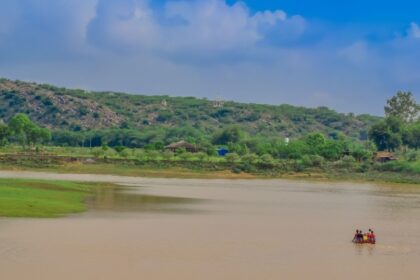 View of Damdama Lake, surrounded by lush green trees and Aravalli hills in Haryana.