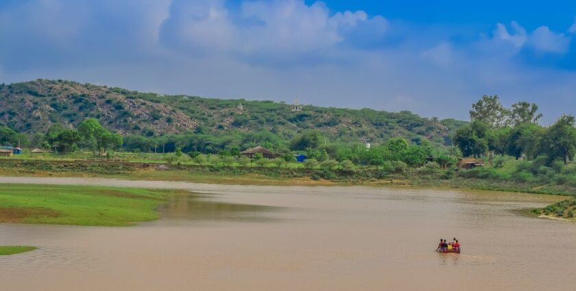 View of Damdama Lake, surrounded by lush green trees and Aravalli hills in Haryana.