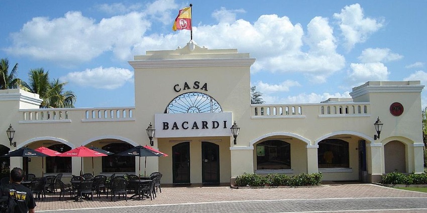 An image of Casa Bacardi visitor center, a flag, and outdoor seating area on a sunny day.