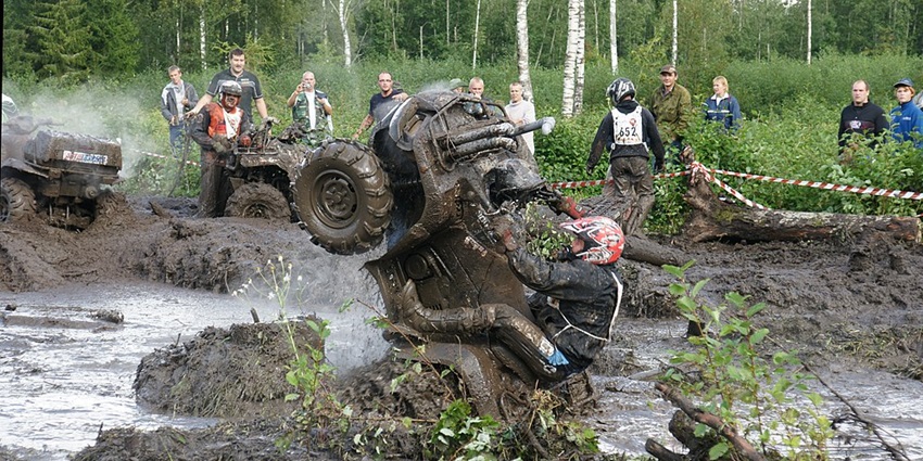 A man soaked in mud rides his ATV through a muddy trail during an off-road race.