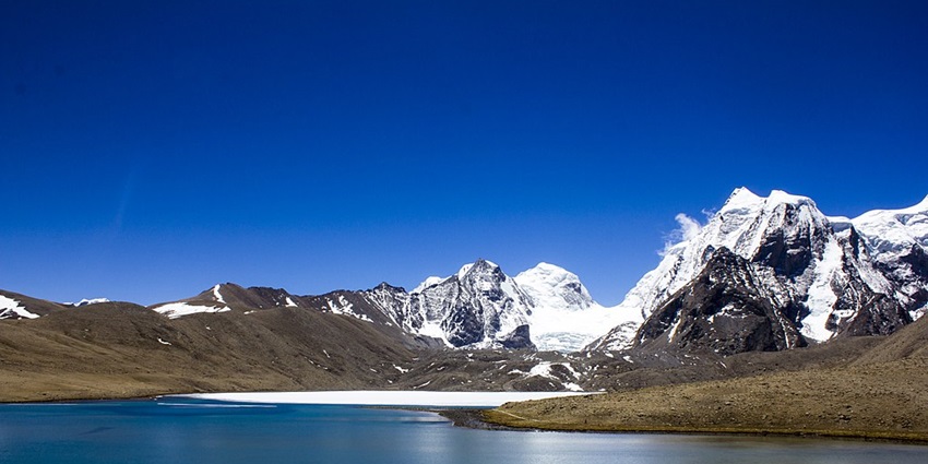 Lake with a still water body surrounded by sandy hills and mountains covered in snow.