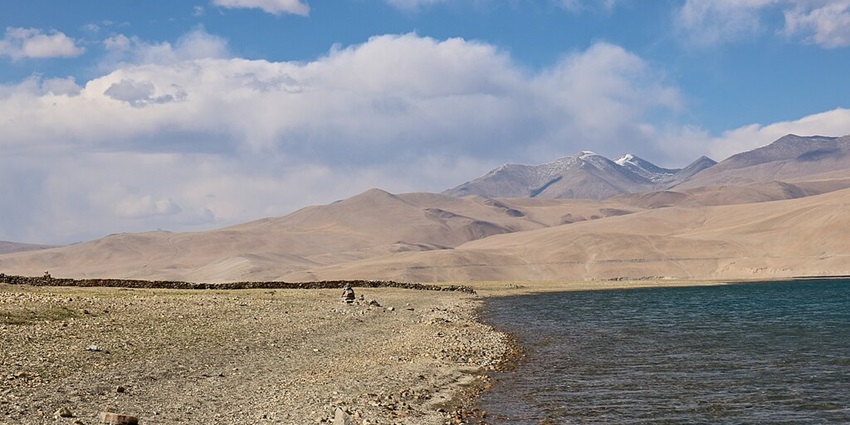 Tso Moriri Lake with its sandy shorelines, a pile of rock and mountains in the back