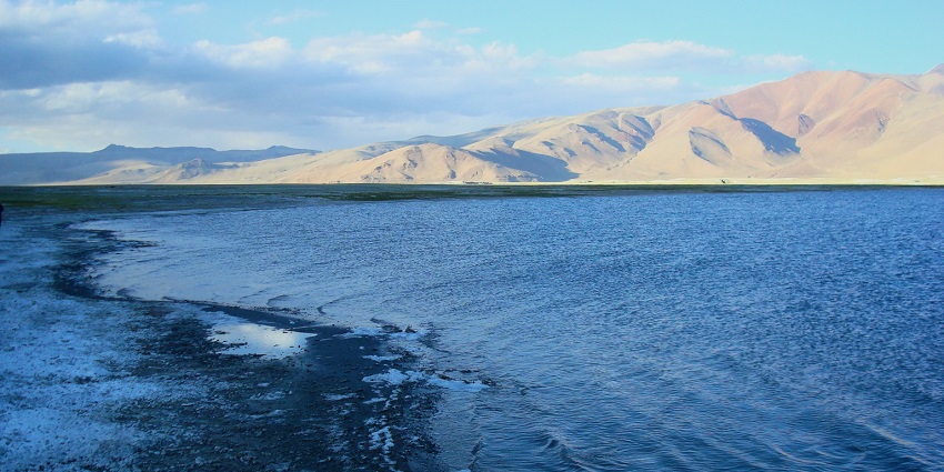Tso Kar Lake with its large water body, frozen shoreline and sandy mountains at a distance