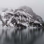 A breathtaking view of Tsomgo Lake surrounded by snow-capped mountains in foggy weather.