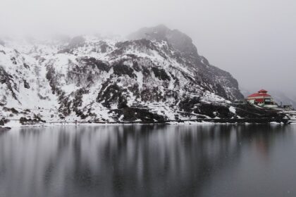 A breathtaking view of Tsomgo Lake surrounded by snow-capped mountains in foggy weather.