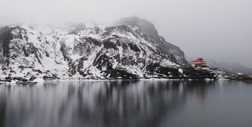 A breathtaking view of Tsomgo Lake surrounded by snow-capped mountains in foggy weather.